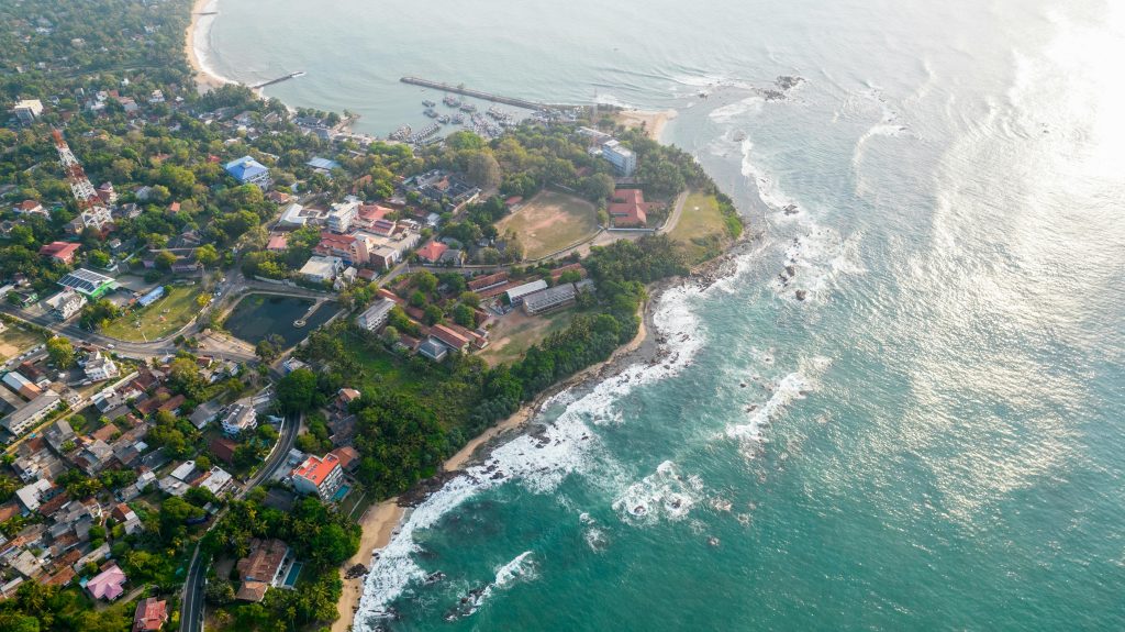 A stunning aerial shot of Tangalle's coastline showcasing lush greenery and vibrant ocean waves.